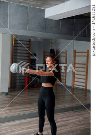 Woman exercises with a kettlebell in a gym setting during the day Woman exercises with a kettlebell in a gym setting during the day 141635251