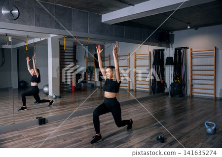 Beauty woman stretching arms during dynamic gym lunge exercise. Pretty woman training indoors with healthy athletic body movement and balance. Fitness wellness concept. Beauty woman stretching arms during dynamic gym lunge exercise. Pretty woman training indoors with healthy athletic body movement and balance. Fitness wellness concept. 141635274
