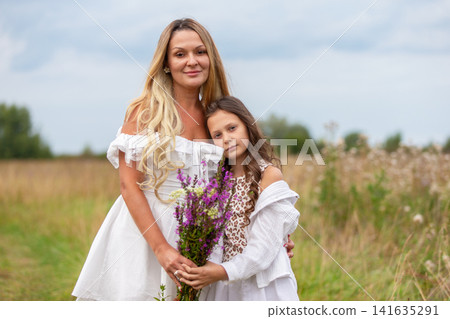 Mother and daughter share a joyful moment in a field with wildflowers on a sunny day Mother and daughter share a joyful moment in a field with wildflowers on a sunny day 141635291