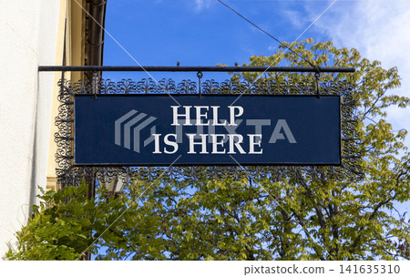 Help is here and support words symbol. Concept words Help is here on beautiful black road sign. Beautiful blue sky green tree background. Business help is here and support concept. Copy space. Help is here and support words symbol. Concept words Help is here on beautiful black road sign. Beautiful blue sky green tree background. Business help is here and support concept. Copy space. 141635310