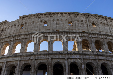 Famous Coliseum in Rome. Colosseum, or Coliseum. Part of the wall of an antique stone structure with arches. Italy, Europe. Famous touristic place in the world, Europe. Beautiful blue sky background. Famous Coliseum in Rome. Colosseum, or Coliseum. Part of the wall of an antique stone structure with arches. Italy, Europe. Famous touristic place in the world, Europe. Beautiful blue sky background. 141635338