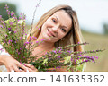 Smiling woman holding wildflowers in a sunny meadow during a warm afternoon 141635362