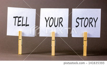 Tell your story symbol. Concept word Tell your story on beautiful white papers on wooden clothespin. Beautiful grey background. Business tell your story concept. Copy space. Tell your story symbol. Concept word Tell your story on beautiful white papers on wooden clothespin. Beautiful grey background. Business tell your story concept. Copy space. 141635393