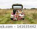 Family picnic in a serene field with a car trunk serving as a seat for a mother and daughter 141635442