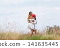 Mother and child enjoying a playful moment outdoors with a red balloon in a grassy field on a cloudy day 141635445