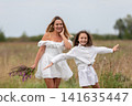 Mother and daughter joyfully playing in a field on a cloudy day with wildflowers 141635447