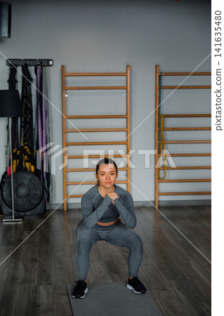 Beautiful woman doing squat exercise on mat in gym wearing sportswear with lower body training and healthy fitness lifestyle concept 141635480