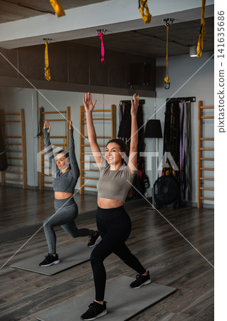 Women practice fitness routines indoors with exercise mats in a gym during daylight hours Women practice fitness routines indoors with exercise mats in a gym during daylight hours 141635686