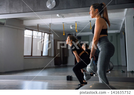 Women exercise with kettlebells in a gym during the day while maintaining focus and proper form Women exercise with kettlebells in a gym during the day while maintaining focus and proper form 141635732