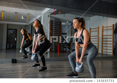 Women exercise with kettlebells in a gym during a workout session in the afternoon, focusing on strength training and fitness Women exercise with kettlebells in a gym during a workout session in the afternoon, focusing on strength training and fitness 141635733