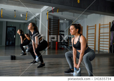 Women lifting kettlebells in gym during workout session for strength training and fitness Women lifting kettlebells in gym during workout session for strength training and fitness 141635734