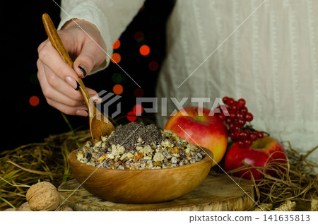 Woman in ukrainian native dresses standing behind table with kutia. Woman in national costume preparing kutya food for Christmas. Woman in ukrainian native dresses standing behind table with kutia. Woman in national costume preparing kutya food for Christmas. 141635813