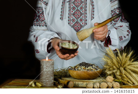 Woman in ukrainian native dresses standing behind table with kutia. Woman in national costume preparing kutya food for Christmas. Woman in ukrainian native dresses standing behind table with kutia. Woman in national costume preparing kutya food for Christmas. 141635815