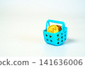 Small blue plastic shopping basket filled with golden dollar coins on a white background. Representing retail, money, savings, wealth, and budget. Minimalist still life for financial concepts. 141636006