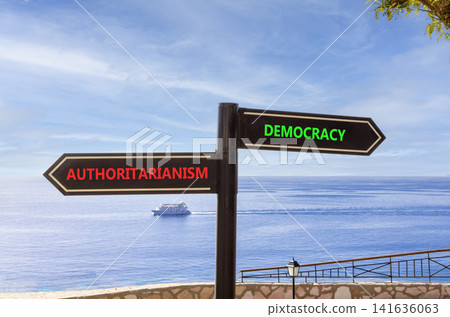Democracy or authoritarianism symbol. Concept words Democracy Authoritarianism on beautiful black road sign. Beautiful blue sky background. Business democracy authoritarianism concept. Copy space Democracy or authoritarianism symbol. Concept words Democracy Authoritarianism on beautiful black road sign. Beautiful blue sky background. Business democracy authoritarianism concept. Copy space 141636063
