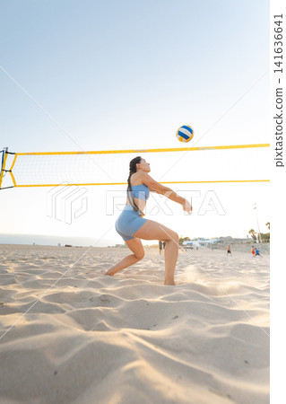 Woman plays beach volleyball under clear sky during sunny day Woman plays beach volleyball under clear sky during sunny day 141636641