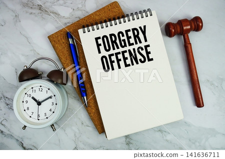 Forgery Offense text written on notepad with pen, alarm clock and judge gavel on marble background Forgery Offense text written on notepad with pen, alarm clock and judge gavel on marble background 141636711