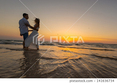 Couple enjoying time together on beach during sunset while waves gently touch their feet Couple enjoying time together on beach during sunset while waves gently touch their feet 141636734