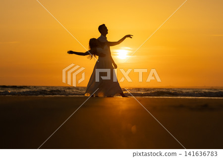 Couple enjoys time together on the beach as the sun sets over the ocean horizon Couple enjoys time together on the beach as the sun sets over the ocean horizon 141636783