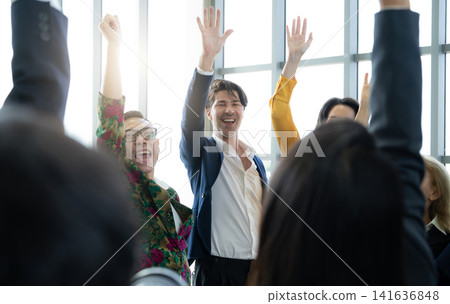 Diverse business professionals raising hands during corporate workshop in modern office, energetic teamwork celebration and leadership training concept with multicultural employee engagement. Diverse business professionals raising hands during corporate workshop in modern office, energetic teamwork celebration and leadership training concept with multicultural employee engagement. 141636848
