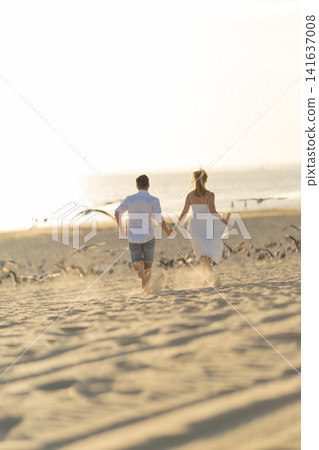Couple walks on beach at sunset while holding hands and enjoying the moment Couple walks on beach at sunset while holding hands and enjoying the moment 141637008