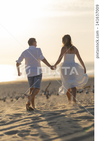 Young couple walks together on the beach during sunset holding hands and enjoying the moment Young couple walks together on the beach during sunset holding hands and enjoying the moment 141637009