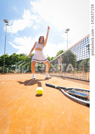 Woman plays tennis on an outdoor court during the day with bright sun shining down Woman plays tennis on an outdoor court during the day with bright sun shining down 141637159
