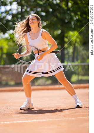 Tennis player practices on clay court in sunny weather during afternoon Tennis player practices on clay court in sunny weather during afternoon 141637162