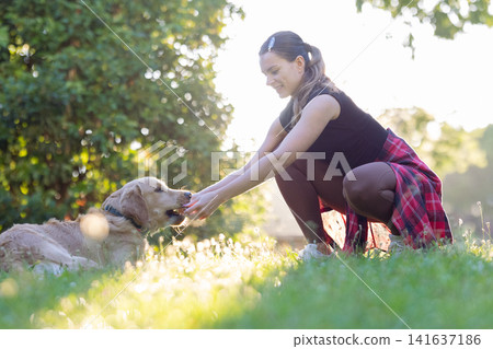 Woman enjoys time with dog while sitting on grass in sunny park during afternoon Woman enjoys time with dog while sitting on grass in sunny park during afternoon 141637186