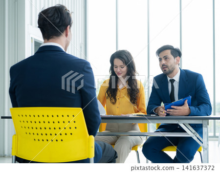Job interview concept. Diverse hr team doing job interview with a man in business office. Human resources team interviewing a potential job candidate. Hiring, employment, and recruitment concept. Job interview concept. Diverse hr team doing job interview with a man in business office. Human resources team interviewing a potential job candidate. Hiring, employment, and recruitment concept. 141637372