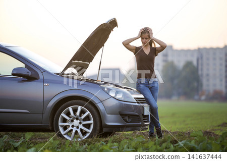 Young woman and a car with popped hood. Transportation, vehicles problems and breakdowns concept. Young woman and a car with popped hood. Transportation, vehicles problems and breakdowns concept. 141637444