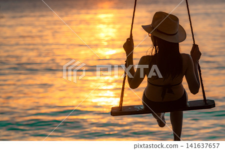 Silhouette woman wear bikini and straw hat swing the swings at the beach on summer vacation at sunset. Enjoying and relaxing girl on holiday. Summer vibes. Woman watching beautiful sunset sky. Silhouette woman wear bikini and straw hat swing the swings at the beach on summer vacation at sunset. Enjoying and relaxing girl on holiday. Summer vibes. Woman watching beautiful sunset sky. 141637657