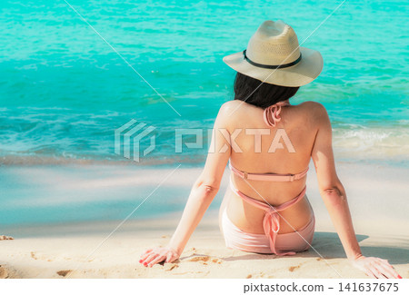 Rear view of woman relaxing on a sandy tropical beach while enjoying the turquoise ocean under a clear blue sky, peaceful summer vacation, luxury resort destination and wellness travel concept. Rear view of woman relaxing on a sandy tropical beach while enjoying the turquoise ocean under a clear blue sky, peaceful summer vacation, luxury resort destination and wellness travel concept. 141637675