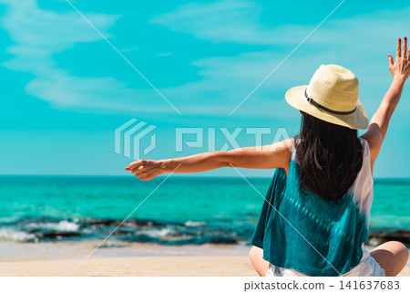 Back view of happy woman raising her arms toward the turquoise tropical ocean on a sunny summer beach. Freedom, wellness lifestyle, travel adventure and vacation. Wellness retreat, travel destination. Back view of happy woman raising her arms toward the turquoise tropical ocean on a sunny summer beach. Freedom, wellness lifestyle, travel adventure and vacation. Wellness retreat, travel destination. 141637683
