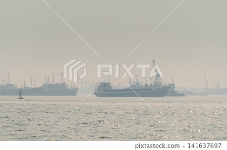 Air pollution and haze covering an industrial harbor with cargo ships. Poor air quality, environmental pollution, industrial emissions and atmospheric contamination. Urban industrial emissions. Air pollution and haze covering an industrial harbor with cargo ships. Poor air quality, environmental pollution, industrial emissions and atmospheric contamination. Urban industrial emissions. 141637697