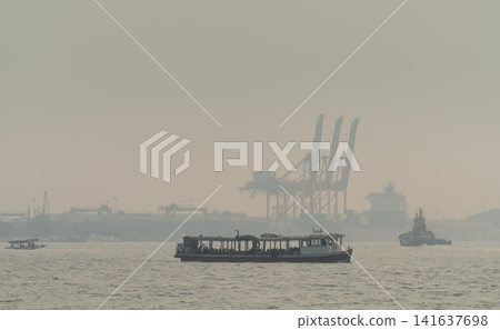 Air pollution and haze covering an industrial harbor with cargo ships. Poor air quality, environmental pollution, industrial emissions and atmospheric contamination. Urban industrial emissions. Air pollution and haze covering an industrial harbor with cargo ships. Poor air quality, environmental pollution, industrial emissions and atmospheric contamination. Urban industrial emissions. 141637698
