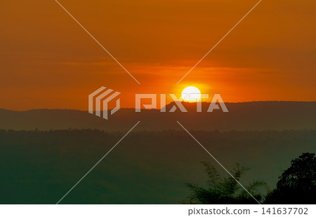 Golden sunrise over layered mountain forest landscape with glowing orange sky. Peaceful natural scenery. Travel, nature, wellness and outdoor adventure concepts. Tranquil nature. travel destination. Golden sunrise over layered mountain forest landscape with glowing orange sky. Peaceful natural scenery. Travel, nature, wellness and outdoor adventure concepts. Tranquil nature. travel destination. 141637702
