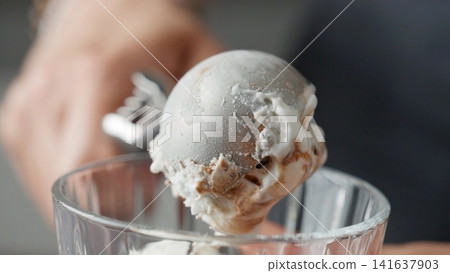 Hands Scooping A Round Portion Of Delicious Ice Cream With Topping Using An Ice Cream Scoop Hands Scooping A Round Portion Of Delicious Ice Cream With Topping Using An Ice Cream Scoop 141637903