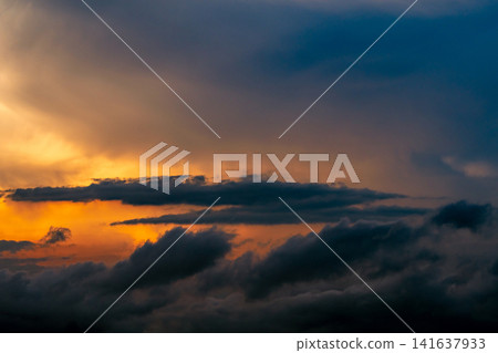 Dramatic cumulonimbus storm clouds illuminated by golden sunset light above dark rain clouds creating an extreme weather sky, atmospheric landscape and climate change background with copy space. Dramatic cumulonimbus storm clouds illuminated by golden sunset light above dark rain clouds creating an extreme weather sky, atmospheric landscape and climate change background with copy space. 141637933
