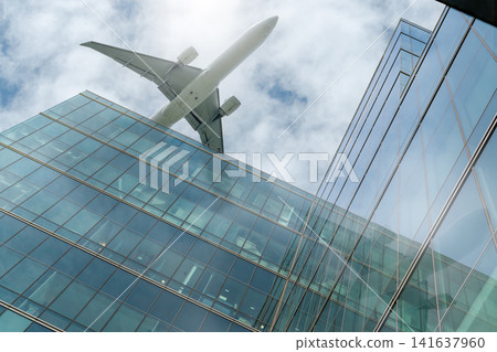 Commercial passenger airplane flying above modern glass office buildings, symbolizing international business travel, corporate aviation, global transportation, urban architecture and modern mobility. Commercial passenger airplane flying above modern glass office buildings, symbolizing international business travel, corporate aviation, global transportation, urban architecture and modern mobility. 141637960