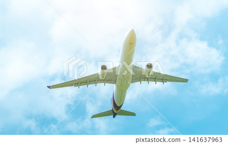 Commercial airline flying on blue sky and white fluffy clouds. Under view of airplane flying. Passenger plane after take off or going to landing flight. Vacation travel abroad. Air transportation. 141637963