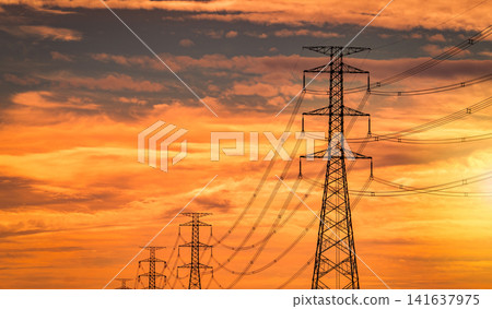 High voltage electricity transmission towers and power lines against dramatic orange sunset sky. Modern energy infrastructure, electrical distribution network, utility grid and reliable power supply. 141637975