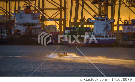 BARCELONA, SPAIN - NOVEMBER 09, 2018 - Container cargo ships and docks with cranes loading and unloading goods and the pilot boat in the sea BARCELONA, SPAIN - NOVEMBER 09, 2018 - Container cargo ships and docks with cranes loading and unloading goods and the pilot boat in the sea 141638079