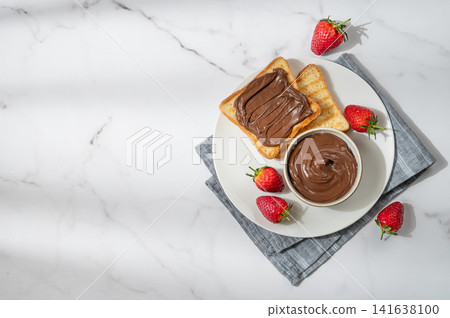 Toasted bread with chocolate cream and strawberry on a plate on a marble background Toasted bread with chocolate cream and strawberry on a plate on a marble background 141638100
