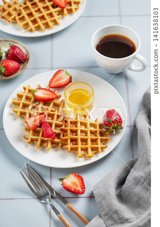 Belgian waffles with fresh strawberries and honey on a white plate on a blue tile background Belgian waffles with fresh strawberries and honey on a white plate on a blue tile background 141638103