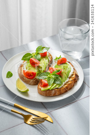 Two avocado toasts with cream cheese, tomatoes, and basil on a tile background Two avocado toasts with cream cheese, tomatoes, and basil on a tile background 141638114