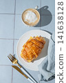 A golden croissant sandwich with ham and cheese on a white plate on a tile background 141638128