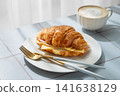 A golden croissant sandwich with ham and cheese on a white plate on a tile background 141638129