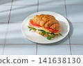 A golden croissant sandwich with ham, cheese, tomato, and arugula on a tile background 141638130