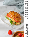 A golden croissant sandwich with ham, cheese, tomato, and arugula on a marble background 141638131